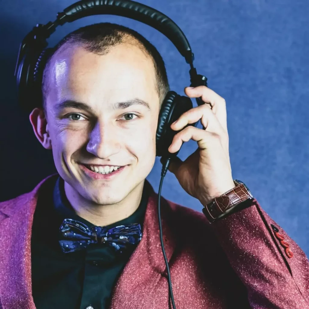 Daniel Wróbel w słuchawkach, uśmiechnięty, w bordowej marynarce