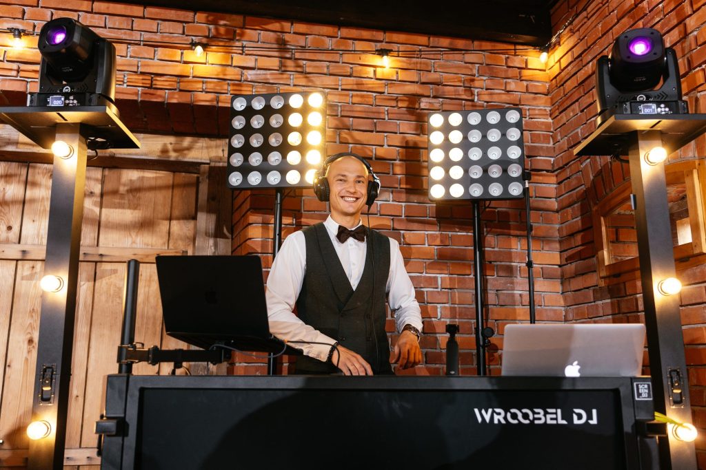 Daniel przy konsolecie WroobelDJ w sali z ceglanymi ścianami, obok ruchome głowy